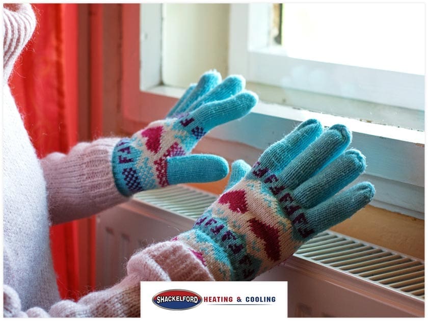 A women wearing gloves in her home holding them over a heater