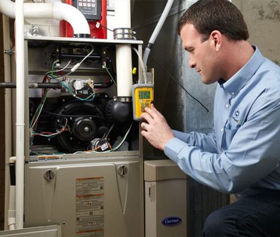 HVAC technician kneeling by an open furnace using testing equipment for repairs