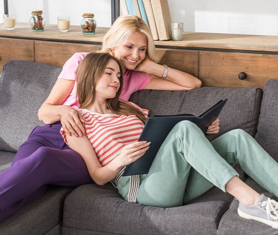 Mother and daughter sitting comfortably on the couch looking at a book