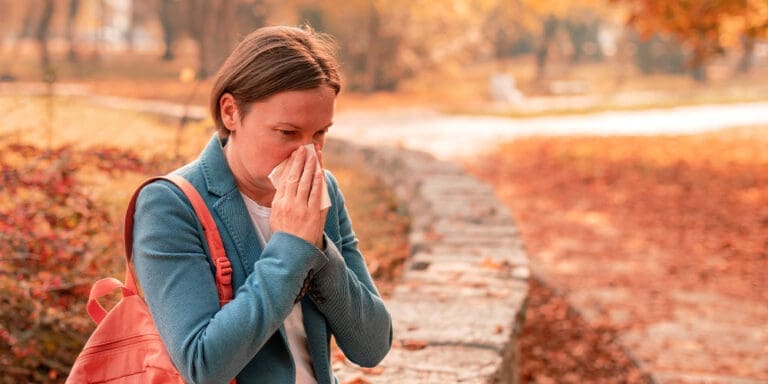 Woman blowing her nose in fall setting.