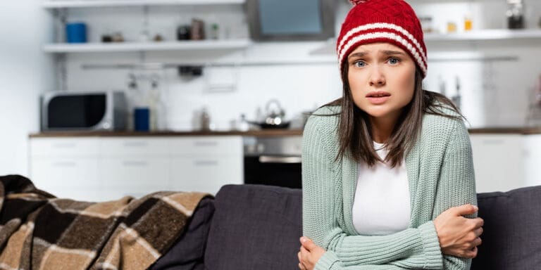 Young woman sitting on couch in hat cold from Furnace not working