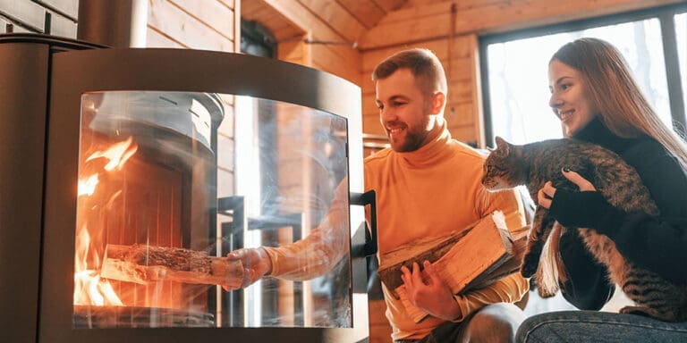 Young couple with a cat putting wood into fireplace.