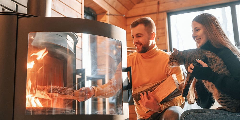 Young couple with a cat putting wood into fireplace.